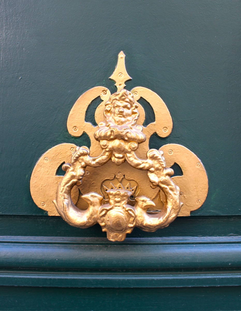 Golden heraldic door knocker on a dark green door