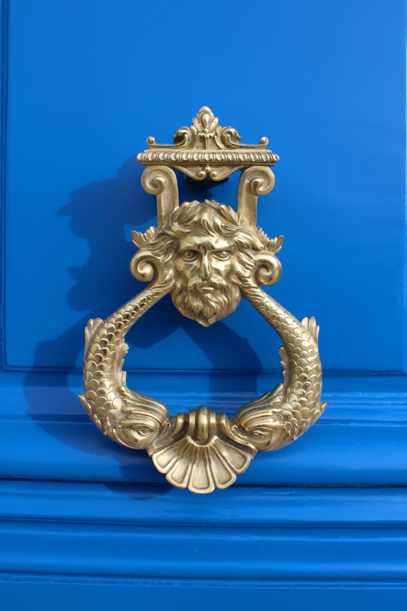 Golden face and fish door knocker on a blue door